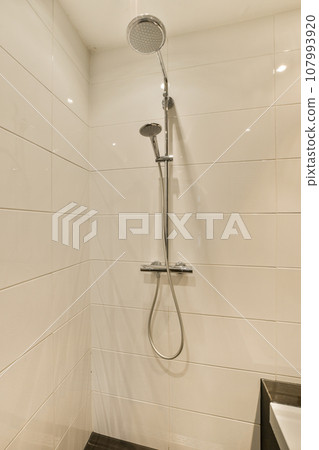 a modern bathroom with white tile walls and black tiles on the floor, there is a shower head in the corner 107993920