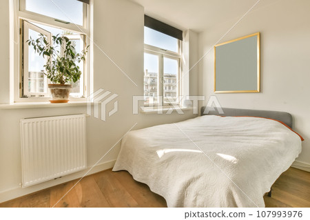 a bedroom with white walls and hardwood flooring the room has a large window that looks out onto the street 107993976
