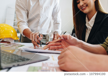 multi ethnic engineer brainstorming and measuring for cost estimating on paperworks and floor plan drawings about design architectural and engineering for houses and buildings. 107994100