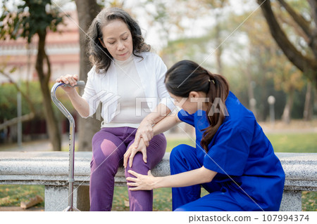 Patient care, female care, young Asian women are taking care of the elderly, providing crutches and walking for patients, and exercising their legs and knees in the park parks 107994374