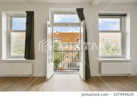 an empty room with two windows and a door leading to the other rooms there is a view of trees outside 107994626