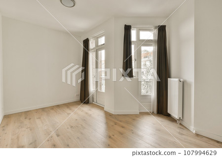 an empty living room with wood flooring and large window looking out onto the street in front of the house an empty living room with wood flooring and large window looking out onto the street in front of the house 107994629