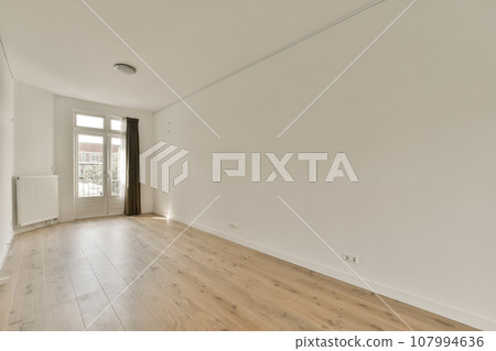 an empty room with white walls and wood flooring on the right side, there is a window to the left 107994636