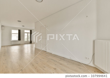an empty room with white walls and wood flooring in the middle part of the room there is a large window 107994641