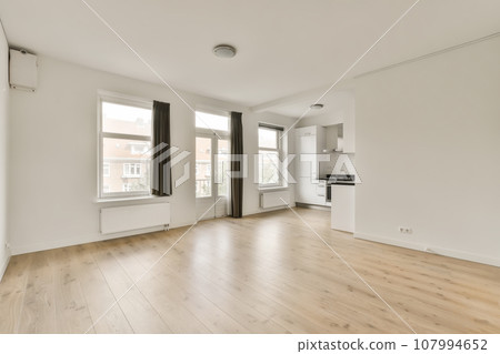 an empty living room with hardwood flooring and white walls, large windows in the room is light wood floors 107994652
