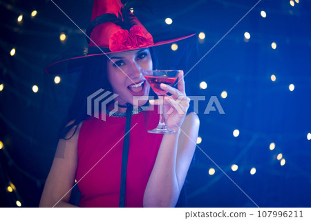 The enchanting essence of Halloween with an image of a woman donning a witch hat, gracefully holding a glass of wine. The enchanting essence of Halloween with an image of a woman donning a witch hat, gracefully holding a glass of wine. 107996211