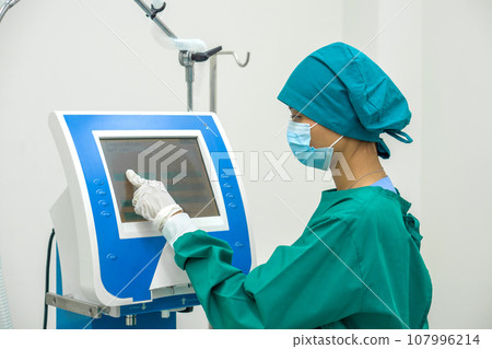 A steadfast surgeon, garbed in sterile surgical attire, is expertly operating an advanced electronic device amidst the high-tech serenity of an operating room. 107996214