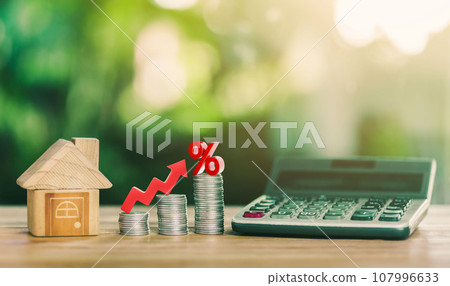 House is placed on the coins. Stacked Coins on wooden table with white illustration shows increasing of interest rates increase. House is placed on the coins. Stacked Coins on wooden table with white illustration shows increasing of interest rates increase. 107996633