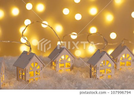 Wooden houses garland string lights on snow and glowing lights bokeh background. Wooden houses garland string lights on snow and glowing lights bokeh background. 107996794
