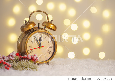 Bronze alarm clock and decorative Christmas tree branch on snow and glowing lights bokeh background Bronze alarm clock and decorative Christmas tree branch on snow and glowing lights bokeh background 107996795