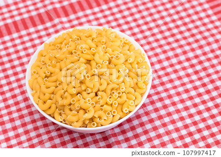 Uncooked Chifferi Rigati Pasta in White Cup on Red Checkered Towel Uncooked Chifferi Rigati Pasta in White Cup on Red Checkered Towel 107997417