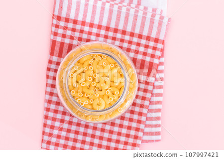 Uncooked Chifferi Rigati Pasta in Glass Jar on Checkered Red Towel 107997421