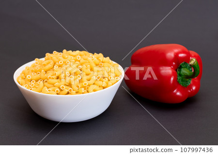 Uncooked Chifferi Rigati Pasta in White Cup and Red Bell Pepper 107997436