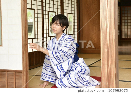 A young woman wearing a yukata on the porch of an old folk house A young woman wearing a yukata on the porch of an old folk house 107998075