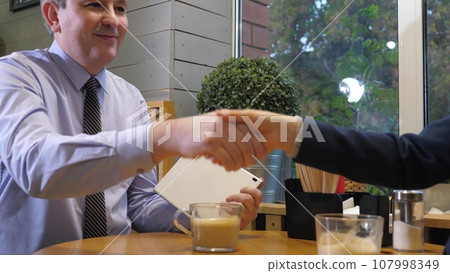Businesspeople check information on tablet and shake hands in cafe. Business meeting of colleagues in company cafe. Businesspeople starts new project resting at work meeting in comfortable cafe 107998349