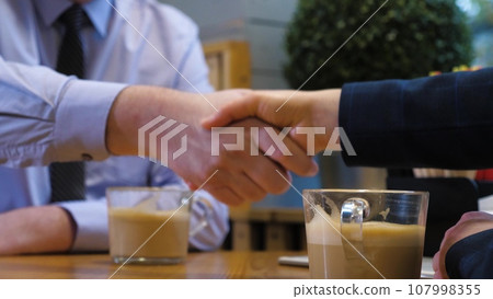 Business partners shake hands celebrating successful deal at meeting in cafe. Businesspeople greeting gesture at informal work meeting in restaurant. Businessman greets lady colleague drinking coffee Business partners shake hands celebrating successful deal at meeting in cafe. Businesspeople greeting gesture at informal work meeting in restaurant. Businessman greets lady colleague drinking coffee 107998355