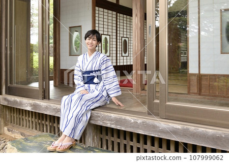 一位穿著浴衣的年輕女子坐在一座古老民宅的門廊上 107999062