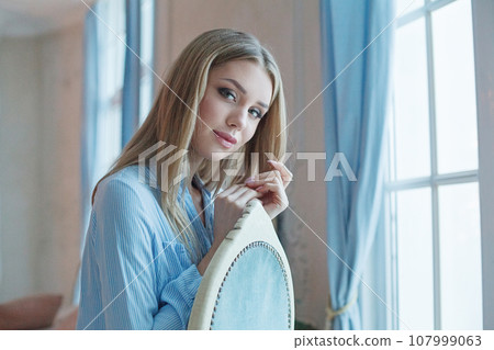 Cute young lady with blonde hair sitting at home, portrait 107999063