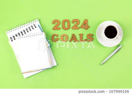 Composition with opened blank notepad and pen, cup of black coffee on a green background. Festive office desktop concept. Morning coffee cup. 2024 goals 107999199
