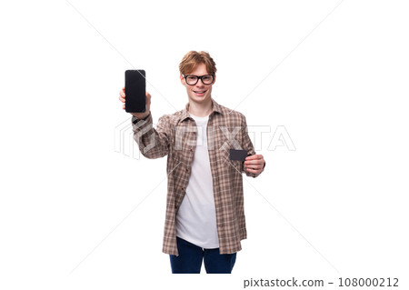 young stylish man with red hair dressed in a summer shirt shows the screen of a vertical smartphone 108000212