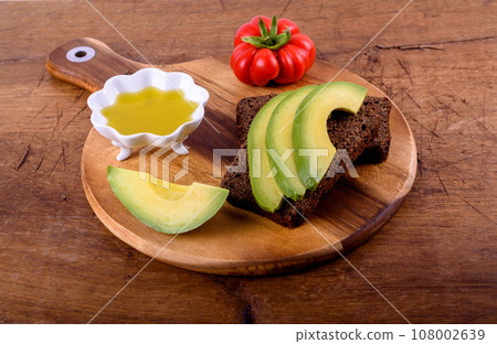 Olive oil, tomato, bread with avocado on wood cutting board. Olive oil, tomato, bread with avocado on wood cutting board. 108002639