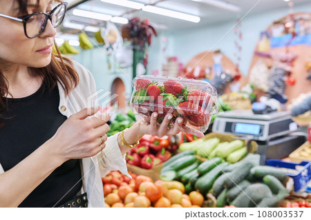 Adult woman choosing buying vegetables fruits berries greens at farmers market 108003537