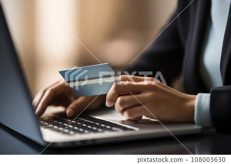 Close-up of female hand holding credit card and laptop making Internet purchase 108003630