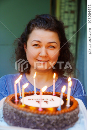 Middle-aged brunette woman with birthday cake with candles. Middle-aged brunette woman with birthday cake with candles. 108004461