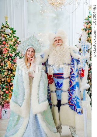 a Father Frost and Snow Maiden in blue costume in the room with christmas trees  108004463