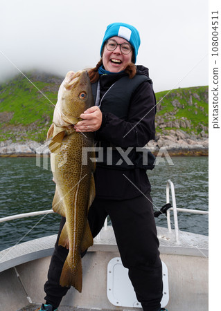 Happy young woman holding big arctic cod. Norway happy fishing. Fisherwoman with cod fish in hands 108004511