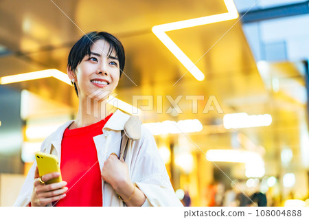 A woman walking in the city with a smartphone 108004888