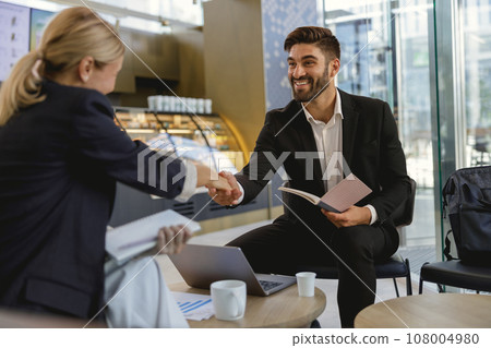 Smiling business partners shaking hands after concluding deal while sitting in cafe Smiling business partners shaking hands after concluding deal while sitting in cafe 108004980