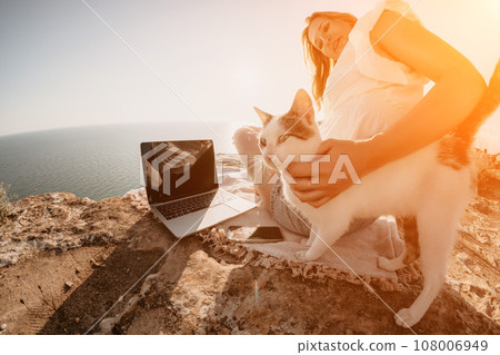 Woman sea laptop. Business woman petting cat and working on laptop by the sea. Close up on hands of pretty lady typing on computer outdoors summer day. Freelance, digital nomad and holidays concept. 108006949