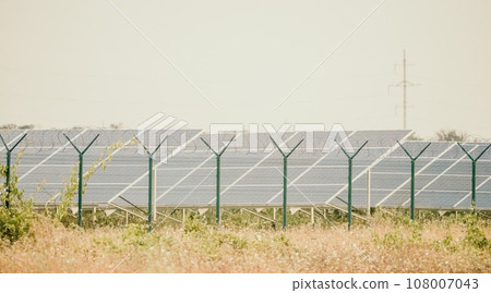Large solar station with blue photovoltaic panels fenced with lattice and barbed wire. Producing clean energy from the sun and minimizing the carbon footprint. 108007043