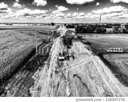 High angle view of a road construction project starting in a corn field and leading into a city.  108007256