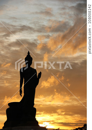 Stand big tall walk Buddha Statue in sun set Light background in park of thailand temple.Yellow orange light silhouette dark shadow of Buddha statue image Lord Buddha. Stand big tall walk Buddha Statue in sun set Light background in park of thailand temple.Yellow orange light silhouette dark shadow of Buddha statue image Lord Buddha. 108008142