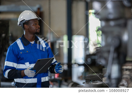 Male African American workers wearing uniform safety and hardhat using tablet working at machine. 108008927