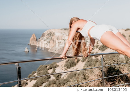 Fitness woman sea. Outdoor workout in park over beach. Female fitness pilates yoga routine concept. Healthy lifestyle. Happy fit woman exercising with rubber band in park. Fitness woman sea. Outdoor workout in park over beach. Female fitness pilates yoga routine concept. Healthy lifestyle. Happy fit woman exercising with rubber band in park. 108013403