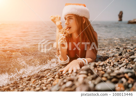 Woman travel sea. Happy tourist enjoy taking picture on the beach for memories. Woman traveler in Santa hat looks at camera on the sea bay, sharing travel adventure journey 108013446