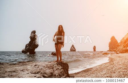 Woman summer travel sea. Happy tourist in hat enjoy taking picture outdoors for memories. Woman traveler posing on the beach at sea surrounded by volcanic mountains, sharing travel adventure journey Woman summer travel sea. Happy tourist in hat enjoy taking picture outdoors for memories. Woman traveler posing on the beach at sea surrounded by volcanic mountains, sharing travel adventure journey 108013467