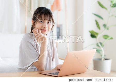 使用一台電腦在客廳裡的年輕女子 使用一台電腦在客廳裡的年輕女子 108015252