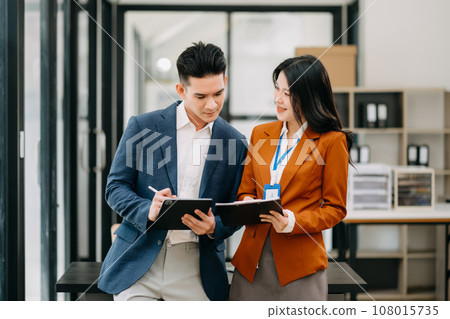 Asian business colleague business presents and explains and using laptop and tablet. Teamwork, financial marketing team, while sitting in office room. Asian business colleague business presents and explains and using laptop and tablet. Teamwork, financial marketing team, while sitting in office room. 108015735