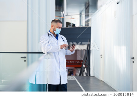 Concentrated male doctor in medical mask working on tablet computer in hospital 108015914