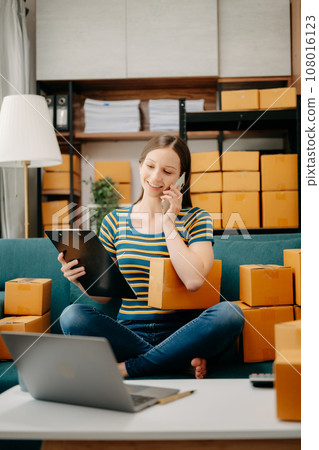 Young business owner woman prepare parcel box and standing check online orders for deliver to customer on tablet, laptop Shopping Online concept. on sofa .. 108016123