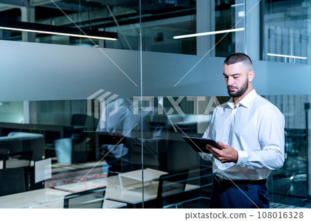 Handsome businessman with digital tablet computer looking in device screen working in modern office. 108016328