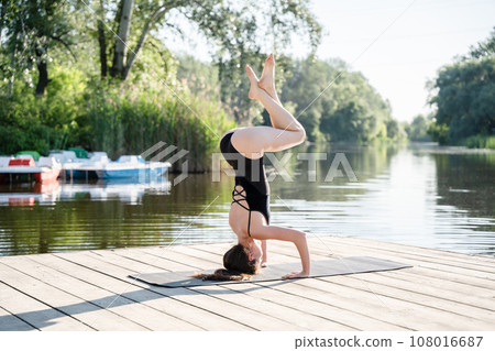 Headstand woman practicing yoga outdoors in the morning by the river. Healthy lifestyle, harmony and balance in body. Headstand woman practicing yoga outdoors in the morning by the river. Healthy lifestyle, harmony and balance in body. 108016687
