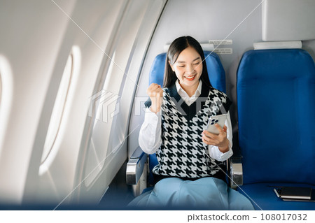 Attractive Asian female passenger of airplane sitting in comfortable seat while working laptop and tablet with mock up area using wireless connection. Travel in style, work with grace.. 108017032