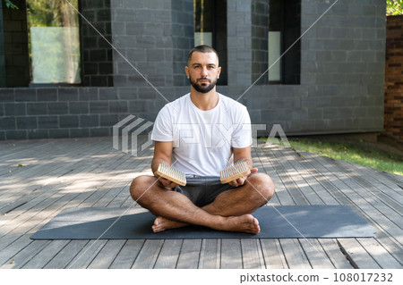Portrait of handsome man holding sadhu boards while sitting in yoga lotus pose Portrait of handsome man holding sadhu boards while sitting in yoga lotus pose 108017232