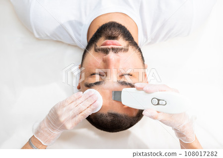 Ultrasonic facial cleansing for young handsome man in professional beauty clinic. View above. 108017282