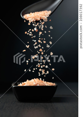 Pink salt is poured into a small black bowl. 108017392